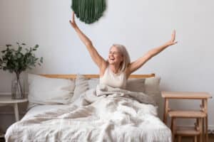 A woman smiling and stretching as she gets out of bed