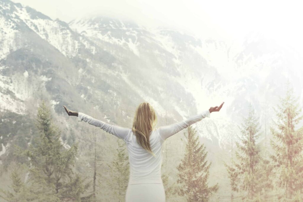 A woman with her back to the camera, spreading her arms wide in front of a mountain.