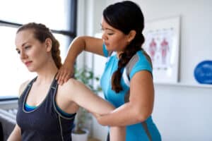 Kinesiologist applying pressure to woman’s shoulder area to examine muscles.