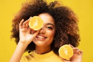 Woman smiling holding up oranges to promote healthy eating habits for overall wellness.
