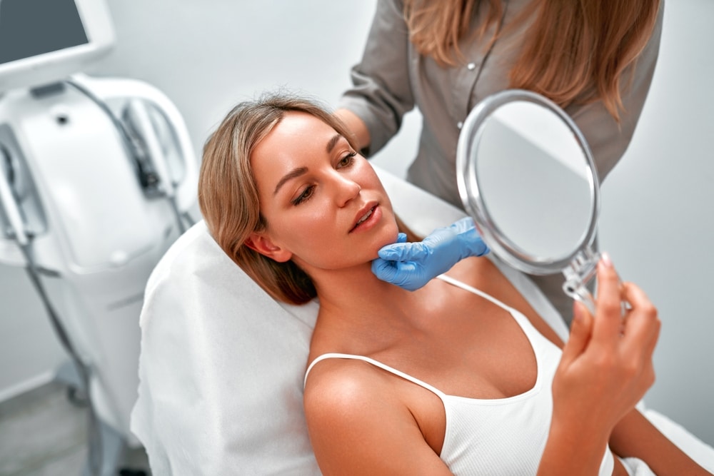 Cosmetologist consulting a woman client in a beauty clinic as she looks in the mirror, preparing for an Aquafirme XS skincare procedure designed to hydrate, exfoliate, and rejuvenate the skin non-invasively.