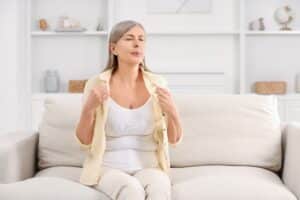 Woman fans herself, looking frustrated with menopause hot flashes