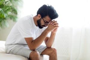 Depressed young man sits on the edge of his bed