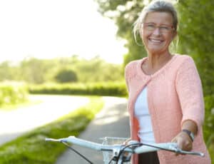 Healthy older woman, smiling widely, rides a bicycle comfortably after starting functional medicine care
