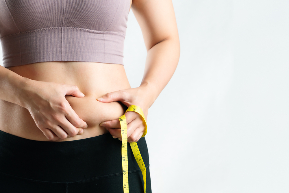 Can Perimenopause Make It Harder to Lose Weight? 1 Woman going through perimenopause pinching stomach fat and holding a tape measure